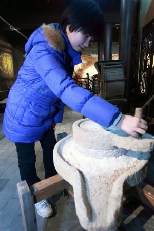 A visitor experiences grinding the grain on an imperial quern stone on display inside the Imperial Granary Museum of Ming Dynasty of Nanxingcang Barn, which has been opened to public visitors, in downtown of Beijing, Jan. 16, 2010. Affluent exhibits reenacting the history of grains transport through the Grand Canal and the imperial barns storage are accessible to visitors, who can also experience the quern of stone mill some 600 years ago. (Xinhua/Luo Wei)