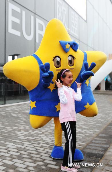 A staff member dressed as the mascot of the Europe Union (EU) poses with a girl in front of the visitors who queue up to enter the Belgium/EU Pavilion at the Shanghai World Expo in Shanghai, east China, June 27, 2010. 