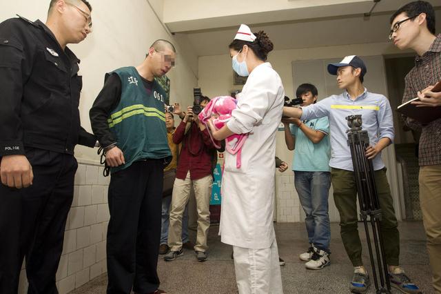 图为嫌疑人在民警的押解下看着自己刚出生的女儿.cfp